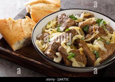 Foie de bœuf frit avec oignons et herbes gros plan dans une assiette et pain sur un plateau en bois horizontal Banque D'Images