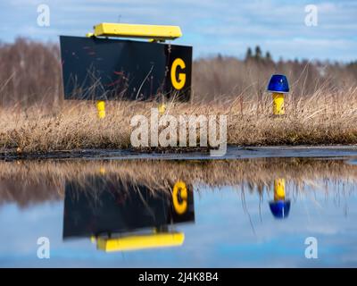 Helsinki / Finlande - 16 AVRIL 2022 : gros plan d'une lumière bleue de la ligne de taxi de l'aéroport avec le signe G du taziway en arrière-plan. Réflexion sur l'eau. Banque D'Images