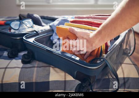 Valise ouverte avec vêtements d'été et lunettes de plongée sur le lit à la maison. Emballage et planification voyage aventure. Banque D'Images