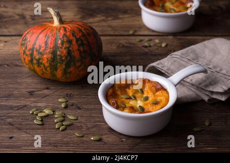 Cocotte de fromage de citrouille en moule céramique avec graines de citrouille et potiron frais sur fond de texture en bois, espace libre, horizontal Banque D'Images