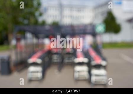 Flou. 3 rangées de chariots sous une verrière sur une place de stationnement de supermarché (kaufland). Arbres et bâtiment en arrière-plan. Vue arrière. Tout sur f Banque D'Images