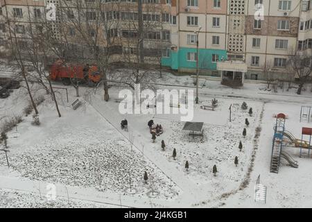 Scène hivernale sur la cour depuis une vue panoramique. Une femme non identifiée joue sur l'aire de jeux avec des enfants. Une femme marche avec un bébé dans une poussette Banque D'Images