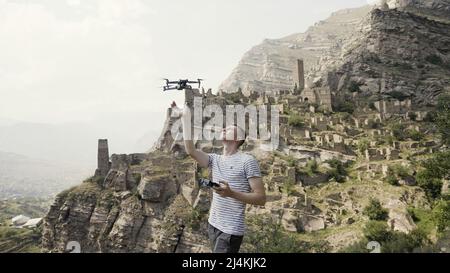 Magnifique paysage d'été. Action. Une vue sur les montagnes et comment un jeune homme lance un petit drone devant le ciel bleu. Banque D'Images