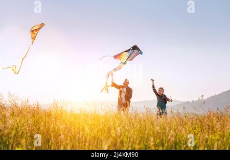 Photo d'été en plein air d'un père souriant avec sa fille qui libère des cerfs-volants colorés sur la prairie haute herbe. Des moments de famille chaleureux ou de plein air Banque D'Images