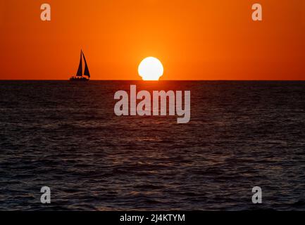 Un voilier le long de la mer dans Un ciel coloré de coucher de soleil Banque D'Images