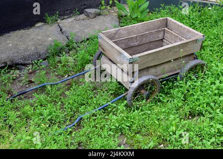 Un petit chariot en bois vide fait maison se trouve dans de l'herbe verte vive Banque D'Images