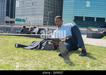 Un jeune homme noir est couché sur une pelouse dans un quartier d'affaires et étudie. Banque D'Images