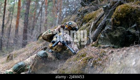 Un soldat des forces spéciales lors d'un affrontement dans la forêt. Il appelle le soutien de son groupe sur le talkie-walkie. Le concept des opérations militaires modernes. Banque D'Images