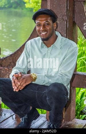 Jour de pluie, un peu brumeux, sensation d'humidité. Dans une chemise à manches longues, une casquette de lierre, un jeune homme noir beau est en piquant près d'un lac dans une pluie, brouillard Banque D'Images