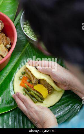 Femme indigène cuisant un plat colombien traditionnel fait avec de la pâte de maïs et farci de poulet, porc, côtes de porc, légumes; enveloppé dans des feuilles de banane. Banque D'Images