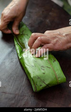 Femme indigène cuisine traditionnelle colombienne plat fait avec de la pâte de maïs et farci avec du poulet, du porc, des côtes de porc, des légumes; enveloppé dans des feuilles de banane, de la vapeur. Banque D'Images