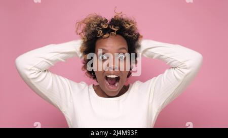 Excitée et surprise femme africaine avec des cheveux bouclés disant wow ayant exprimé l'étonnement, étant fascinant. Studio tourné sur un mur rose. Banque D'Images