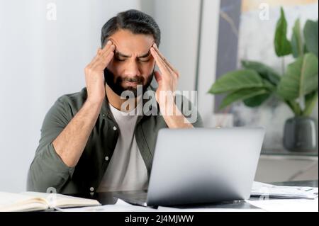 Travailleur de bureau indien ou arabe surtravaillé fatigué, directeur d'une entreprise, assis à un lieu de travail dans le bureau, movie ses temples, fermé ses yeux, souffre de maux de tête, migraine, les besoins reposent sur le travail Banque D'Images