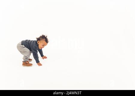 Curieux petit garçon biracial essayant de se lever en studio sur fond blanc. Concept de développement de l'enfant. Photo de haute qualité Banque D'Images