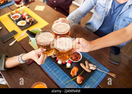 Groupe d'amis méconnaissables qui boivent et toaster de la bière au bar-restaurant de la brasserie. Concept d'amitié avec les jeunes qui s'amusent ensemble Banque D'Images
