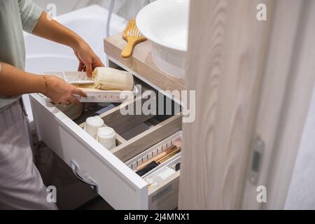 Vue de dessus de femme rangement des mains articles de toilette et articles de toilette dans le tiroir de la salle de bains. Banque D'Images