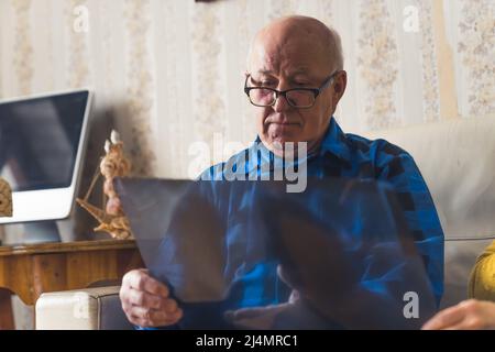 Inquiet vieux bald ridé dans une chemise en flanelle bleu et des lunettes noires regardant sa radiographie et se préoccupant de sa santé. Photo de haute qualité Banque D'Images