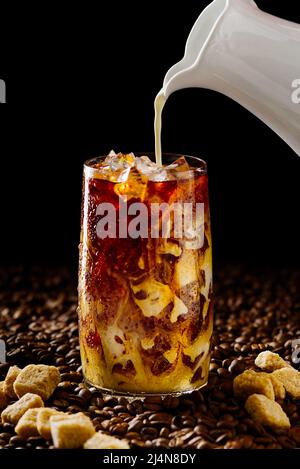 Café glacé. Délicieux café glacé au lait, boisson froide au verre avec glace sur fond de café sombre. Banque D'Images
