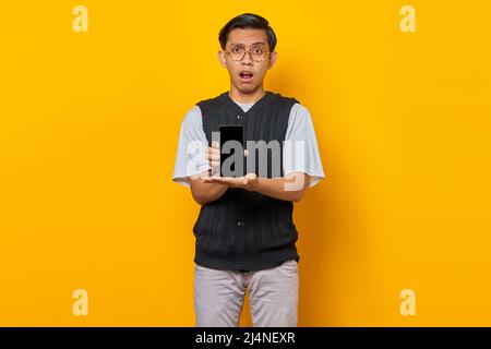Un homme asiatique choqué montrant un écran de smartphone vierge avec paume. Concept de promotion de produit Banque D'Images