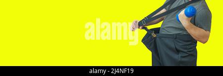 L'homme tire son grand pantalon à sa taille et tient une haltère. Montre comment il a perdu du poids. Banque D'Images