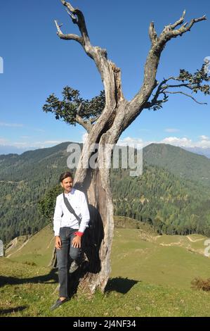 Un jeune touriste mâle se posant contre l'arbre avec une belle vue sur la montagne et le ciel Banque D'Images