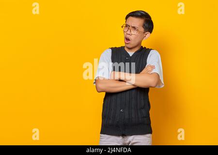 Portrait d'un jeune asiatique surpris avec bras croisés isolé sur fond jaune Banque D'Images