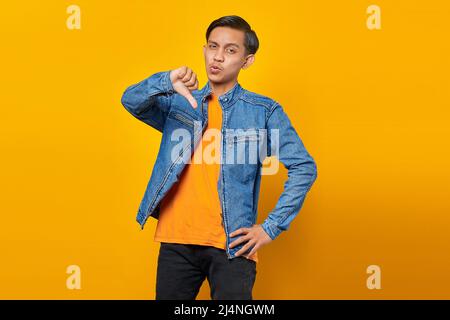 jeune homme asiatique à l'air malheureux montrant le rejet avec le pouce vers le bas geste Banque D'Images
