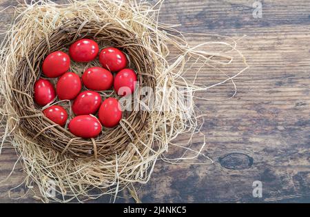 Œufs rouges. Copier l'espace. Pose à plat. Œufs peints en rouge traditionnels posés dans un décor de nid de paille pour la fête de Pâques orthodoxe de l'est. Image de stock. Banque D'Images