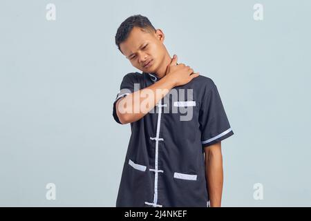 Portrait d'un jeune homme asiatique portant un uniforme de karaté souffrant de douleurs au cou et touchant le dos avec les mains sur fond gris Banque D'Images