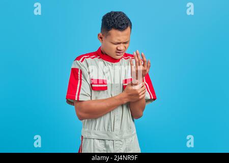 Portrait d'un jeune mécanicien asiatique souffrant de douleurs entre les mains et les doigts sur fond bleu Banque D'Images