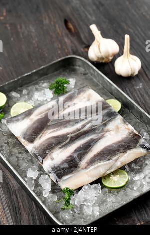 Filet de poisson-chat congelé filet de Lele sur plateau avec lime en tranches et glace pilée, Soft Focus sur table en bois Banque D'Images