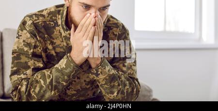 Un jeune vétéran militaire déprimé qui a le PTSD assis sur un canapé et pensant à la guerre Banque D'Images