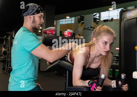 L'entraînement dirigé par un instructeur aide un beau client à effectuer des exercices dans un club de remise en forme, le concept de jouer du sport avec un loisir professionnel de gym Banque D'Images