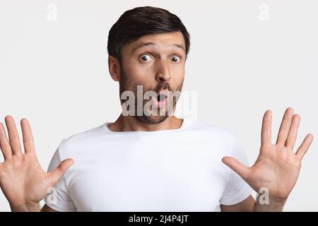 Homme effrayé montrant ses mains regardant la caméra, arrière-plan blanc Banque D'Images