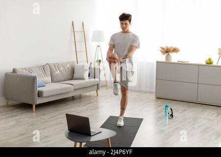 Un homme asiatique se tenant debout du genou à la poitrine en utilisant un ordinateur portable Banque D'Images