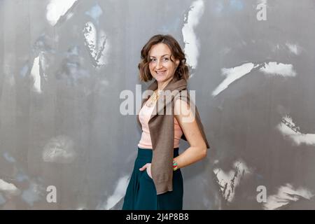 Fille tendance et élégante posant dans des mottes vertes, un chemisier et un pull contre un mur gris Banque D'Images