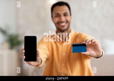 Homme excité montrant un écran de téléphone portable vierge et une carte de crédit Banque D'Images