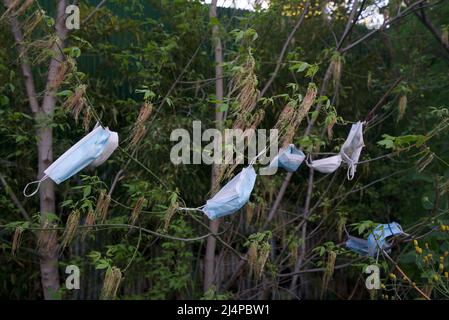 Des dizaines de masques de protection individuelle provenant de la pandémie de Covid-19/coronavirus pendent dans les arbres et les buissons, car les déchets de covid génèrent de la litière. Pollution des revêtements de visage Banque D'Images