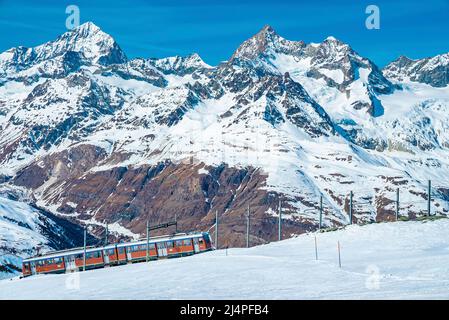 Vue sur l'escalade en train rouge jusqu'à la gare de gornergrat contre la chaîne de montagnes Banque D'Images