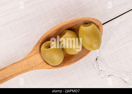 Quelques olives vertes bio piquantes et savoureuses et épicées et une cuillère en bois, sur fond de bois peint blanc naturel, vue du dessus. Banque D'Images