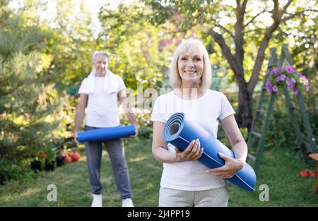 Portrait d'une femme âgée active posant avec son mari dans le jardin, tenant des tapis de yoga, s'exerçant ensemble à l'extérieur Banque D'Images