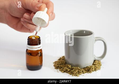 bouteille compte-gouttes d'huile de marijuana dans les mains de l'homme avec gobelet à perfusion, marijuana écrasée, fond blanc Banque D'Images