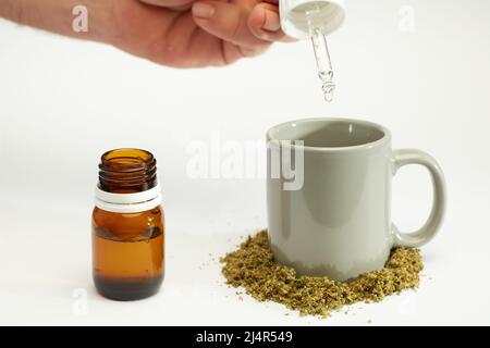 bouteille compte-gouttes d'huile de marijuana dans les mains de l'homme avec gobelet à perfusion, marijuana écrasée, fond blanc Banque D'Images