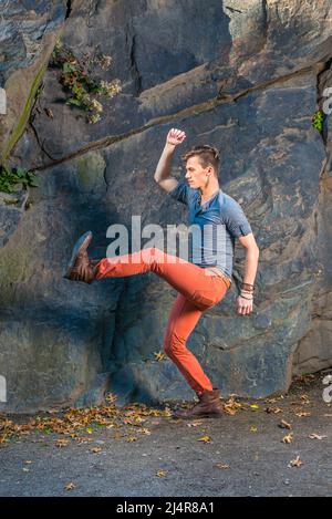 Robe dans un gris manches longues avec un t-shirt de Henley à patte rouillée, jeans rouges, chaussures de bottes en cuir marron, un jeune homme est étirant les jambes, probablement robot de marche Banque D'Images