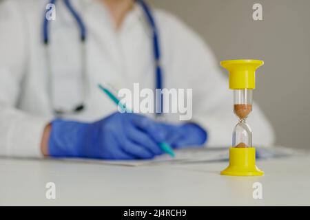 HourGlass avec le temps qui s'est écoulé et le médecin en laboratoire manteau prenant des notes ou une prescription dans le journal. Banque D'Images