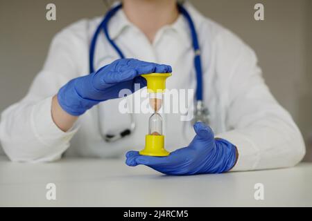 Heures de travail supplémentaires du travailleur médical. Médecin en gants bleus tient un sablier. Banque D'Images