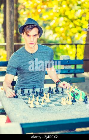 Homme jouant aux échecs. Vêtu d'un maillot Henley à manches longues grises et patte roulantes, un jeune homme adorable joue aux échecs avec un chapeau Fedora en laine Banque D'Images