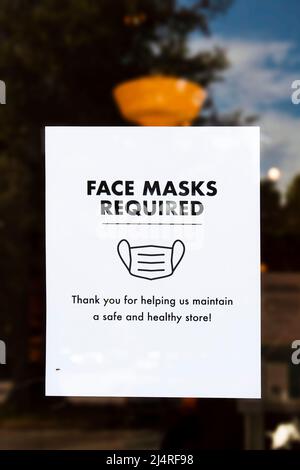 Masque de visage requis signe sur la porte du magasin avec reflet du ciel et des arbres autour de lui et le bug rampant sur elle Banque D'Images