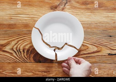 Vue de dessus sur une plaque blanche brisée et main humaine tenant une pièce sur fond en bois. Banque D'Images