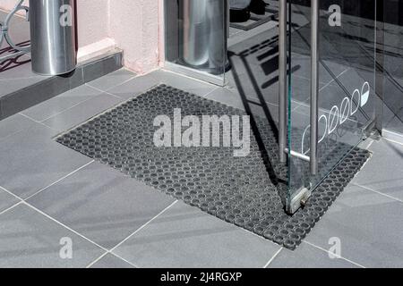 seuil en carreaux de pierre en céramique grise à l'entrée pour le magasin avec tapis de pied en caoutchouc et porte en verre ouverte avec poignée en métal et boucles de fixation au niveau de l'offic Banque D'Images